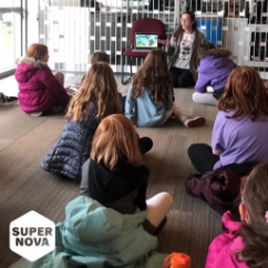 A instructor teaching a bunch of young girls sitting on the carpet.